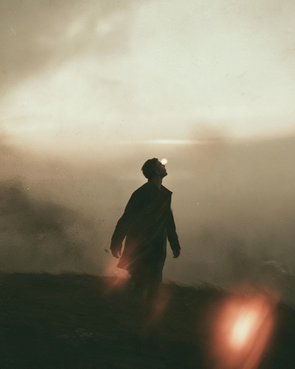 A man walking alone through morning fog, lit from behind.